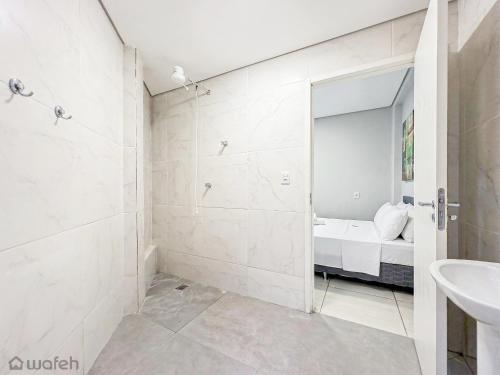 a white bathroom with a bed and a mirror at Wafeh Fleming Suítes Pampulha in Belo Horizonte