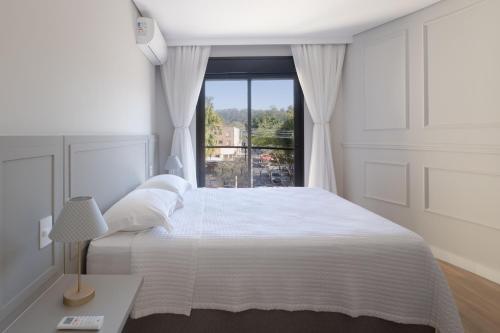 a white bedroom with a large bed and a window at 1986 Apparts in Águas de São Pedro