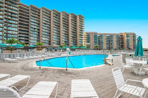 a swimming pool with white chairs and a large building at Sea Colony - 902 Georgetowne House in Bethany Beach
