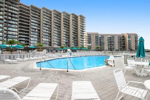 a swimming pool with white chairs and a large building at Sea Colony - 55006 Pine View Rd in Bethany Beach