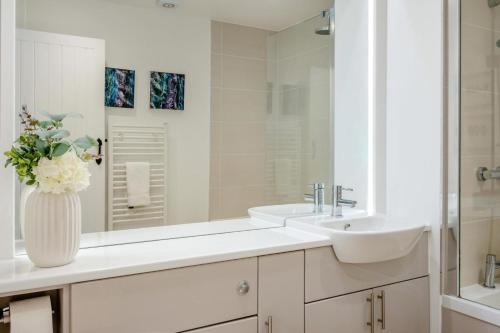 a white bathroom with a sink and a vase of flowers at Smugglers Hide in Beadnell