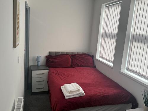 ein Schlafzimmer mit einem roten Bett, auf dem zwei Handtücher liegen in der Unterkunft PLUS Properties Dike 3 Ensuite in Stoke on Trent