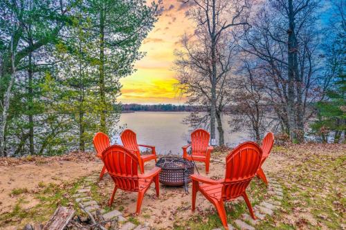 four red chairs around a fire pit next to a lake at A Place To Gather in Tomahawk