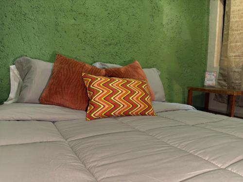 a bed with two pillows on it with a green wall at Hostal el Alebrije in Valle de Bravo