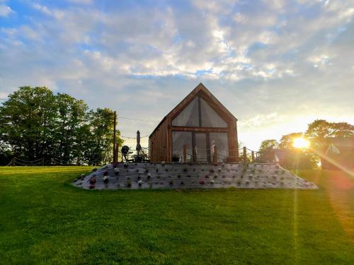 a small wooden building on a field with the sun setting at Mazurskie Stodoły in Piecki
