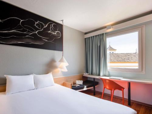 a hotel room with a bed and a desk and a window at Ibis Sevilla in Seville