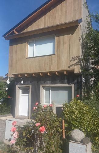 a house with two windows and flowers in front of it at Cabaña con costa de arroyo in San Martín de los Andes
