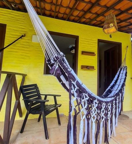 a hammock and a chair in front of a yellow house at Eco Hostal Yuaiurú 2 in Trairi