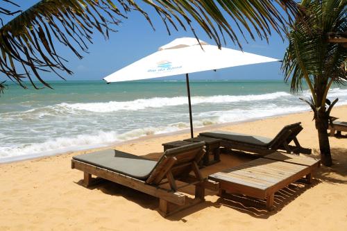 uma mesa e cadeiras e um guarda-sol na praia em Rio Da Barra Villa Hotel em Trancoso