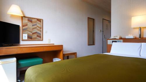 a bedroom with a bed and a desk with a television at Hotel New Gaea Itoshima in Itoshima