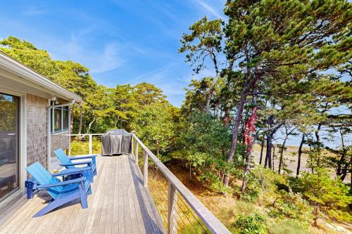 a deck with two blue chairs and trees at Drummer Cove Retreat in Wellfleet
