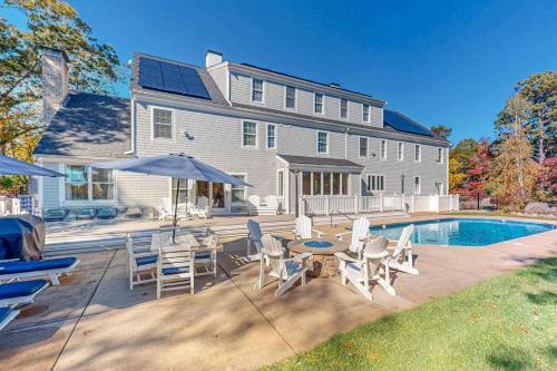 a house with a swimming pool and a patio with chairs and a table at Plum Paradise in Barnstable