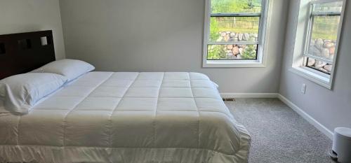 a white bed in a bedroom with two windows at River Valley Stay in Eagan