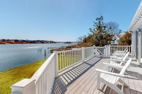 a wooden deck with white chairs and the water at Island Bay Bungalow in Eastham