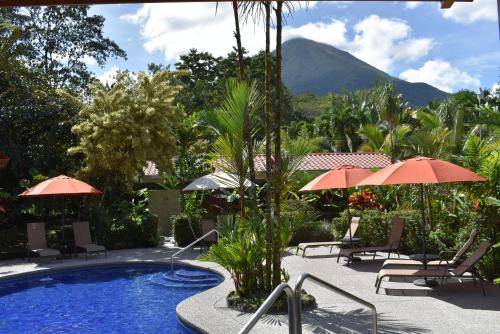 una piscina con sillas, sombrillas y una montaña en Hotel Roca Negra Del Arenal, en Fortuna