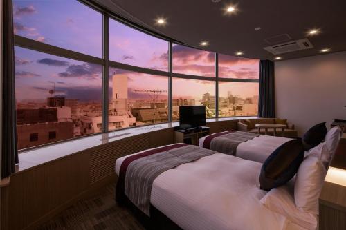 two beds in a room with a view of a city at HOTEL MYSTAYS Tachikawa in Tachikawa