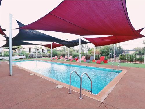 una piscina con una sombrilla roja y negra sobre ella en Capricorn Village, en Newman