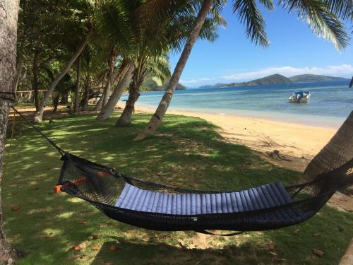 a hammock hanging from two palm trees on a beach at Oneta Resort in Ono Island