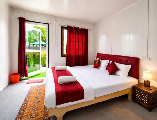 a bedroom with a large bed with red curtains at Snowpeak Retreat in Hundar