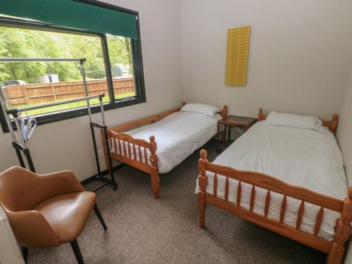 two beds in a room with a chair and a window at Cabin No 15 - Salt and Fern Cabins in Port Talbot