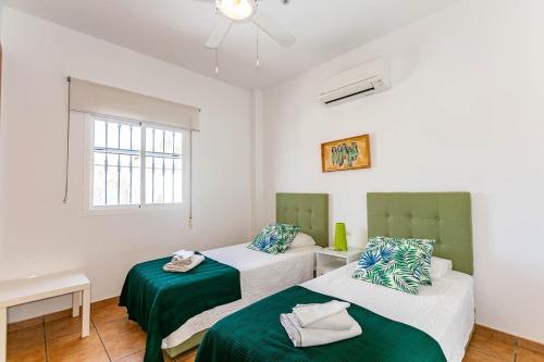 a bedroom with two beds with green sheets and a window at Casa Verdejo in Cómpeta