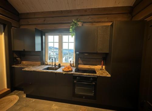 a kitchen with black cabinets and a sink and a window at Log cabin in Hodlekve with mountain view in Sogndal