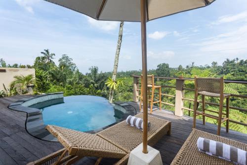 a deck with a pool and chairs and an umbrella at The Scape Valley Villas in Tampaksiring
