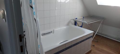 a white tiled bathroom with a tub and a shelf at Location vacances in Cucq