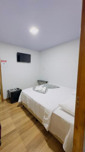 a bedroom with a white bed with a television on the wall at Hotel Luxx Sorriso in Sorriso