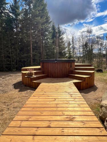 a wooden boardwalk leading to a hot tub in a forest at ARKA Puhkemajad in Päidre
