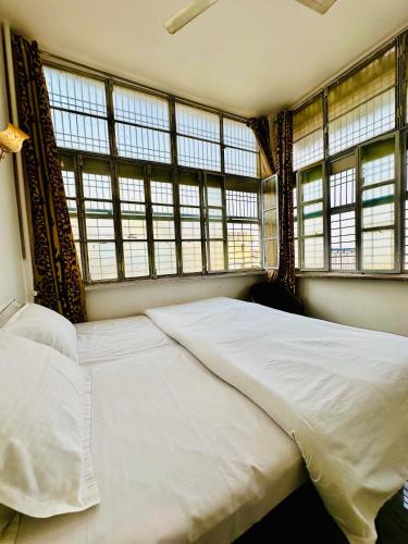 a bedroom with a large white bed with windows at Om Rest House by Bunny Cafe Varanasi in Varanasi