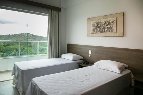 two beds in a hotel room with a window at Peçanha Grande Hotel in Peçanha