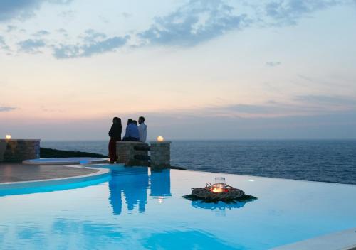 a group of people standing next to a swimming pool overlooking the ocean at Toxotis Villas in Armenistis