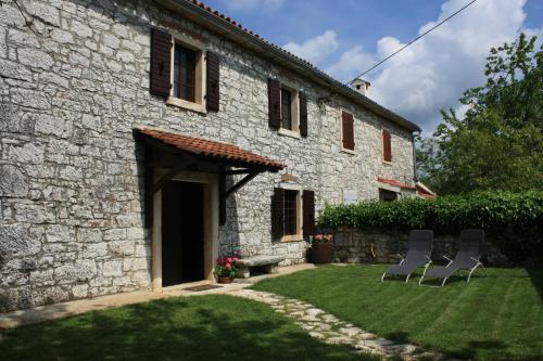 une maison en pierre avec 2 chaises dans la cour dans l'établissement House Kisic, à Višnjan