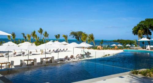 a pool with white umbrellas and chairs and the ocean at Azuri Appartements De Luxe in Roches Noires