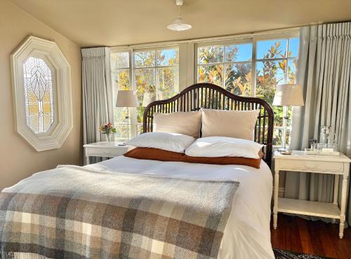 a bedroom with a large bed with two windows at The Vicarage Boutique Bed and Breakfast Oamaru in Oamaru