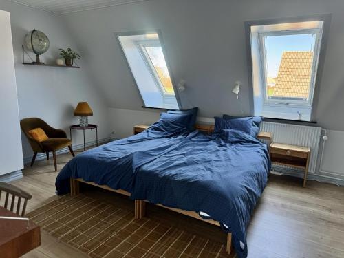 a bedroom with a bed with blue sheets and two windows at Groland Bornholm B&B in Pedersker