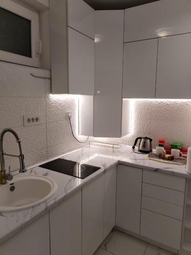 a kitchen with white cabinets and a sink and a mirror at Bella apartman in Mladenovac