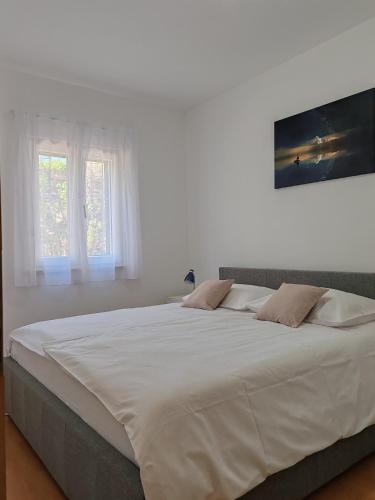 a large white bed in a white room with two windows at Apartments Borovina in Bol