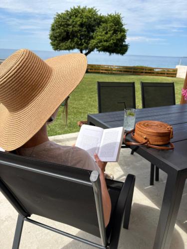 a woman in a straw hat reading a book at a table at Cedrus-Seafront Ionian Stay in Agios Georgios