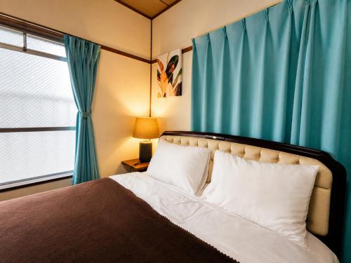 a bedroom with a bed with blue curtains and a window at DiDi Calm 105 in Tokushima