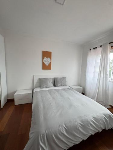 a white bedroom with a large bed and a window at Varanda do Coura in Caminha