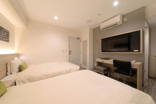 a hotel room with two beds and a desk and a tv at Vessel Inn Shinsaibashi in Osaka