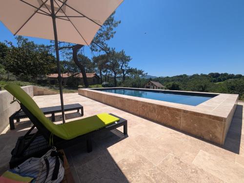 a patio with a chair and an umbrella next to a swimming pool at maison et table d'hôtes Xori Kanta in Ascain