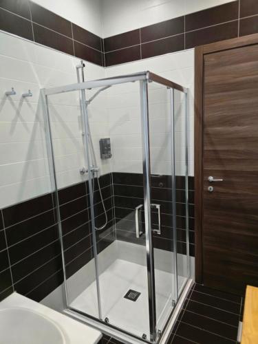 a glass shower in a bathroom with black tiles at Arzella Beachfront Guesthouse in Birżebbuġa