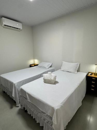 two beds with white sheets and a basket on top at University Suítes in Carmópolis