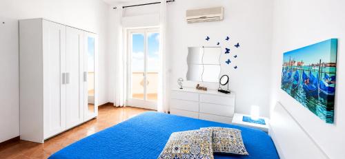 a white bedroom with a blue bed and a window at Dune Dorate,Tramonti Infiniti la tua oasi di pace in Dune ! Aprile al Mare in Appartamento con vista panoramica e WiFi Casa Vacanza Vista Mare in Sicilia Relax e Tramonti Unici in Alcamo Marina