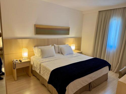 a bedroom with a large bed with two lamps and a window at Flat Mont Blanc Premium in Ribeirão Preto