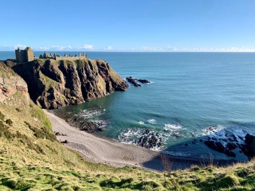 a beach with a castle on top of a cliff at The Auld Bakehouse in Stonehaven
