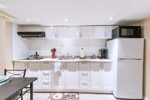 a kitchen with white cabinets and a white refrigerator at St Clair Hotel - Cozy Basement Suite with Parking in Toronto